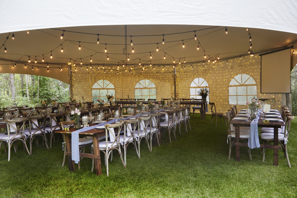 An outdoor wedding reception complete with tables, chairs, and a tent providing shade